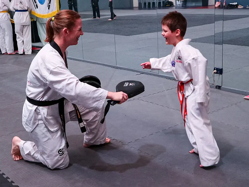 A female instructor holding a kick pad for a Little Dragons student practicing kicks at ATI.