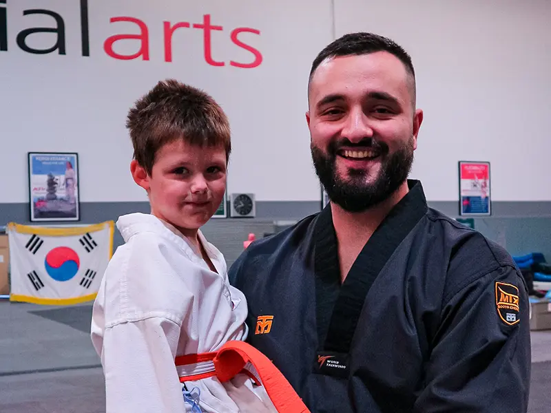 An instructor smiling while holding a young Little Dragons student at ATI Martial Arts.